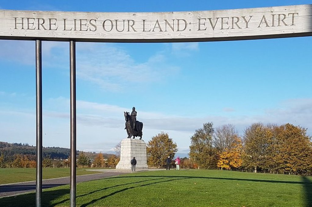 The Bannockburn Memorial in Stirlingshire with a sign depicting the words Here lies our land. in the background is the iconic Robert the Bruce statue.