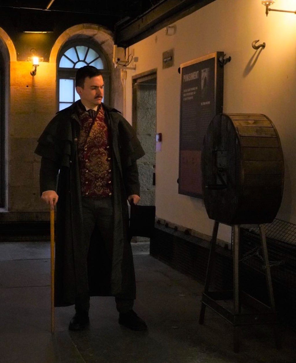 A man standing in period clothing in front of a historic wooden box which was some form of punishment.