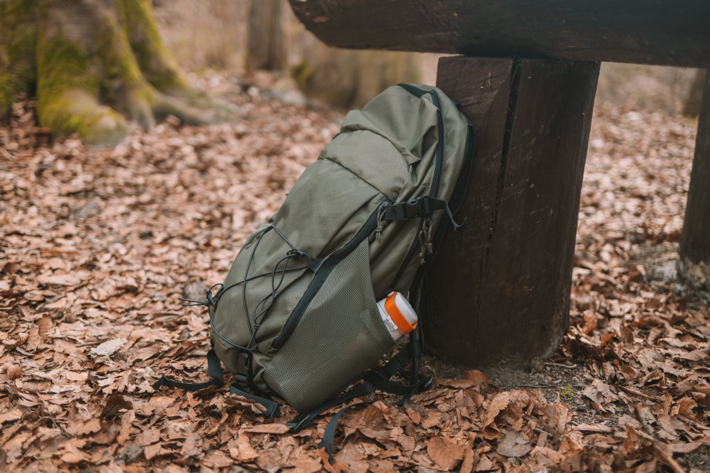 A backpack is resting in Autumn leaves next to a bench on a hiking trail.