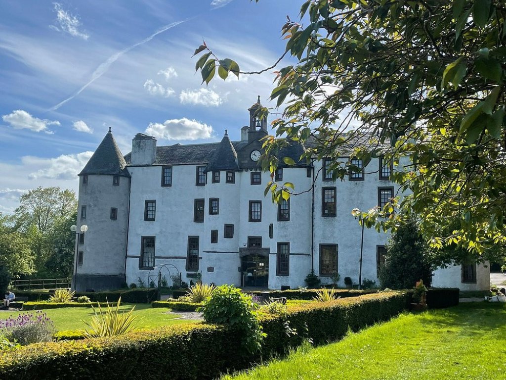 Medieval-style Dudhope Castle with turrets rising above lawns and trees on a sunny day.