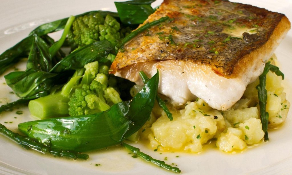 a delicious looking piece of fish sat on a bit of potatoes with fresh broccoli and green veg.