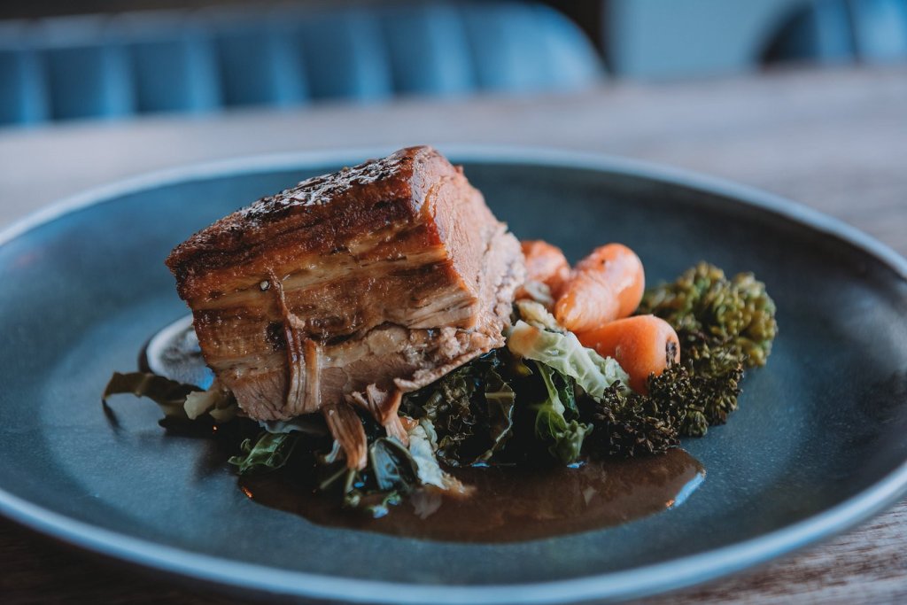 a delicious plate of food, including Pork with baby carrots, kale and broccoli with gravy.