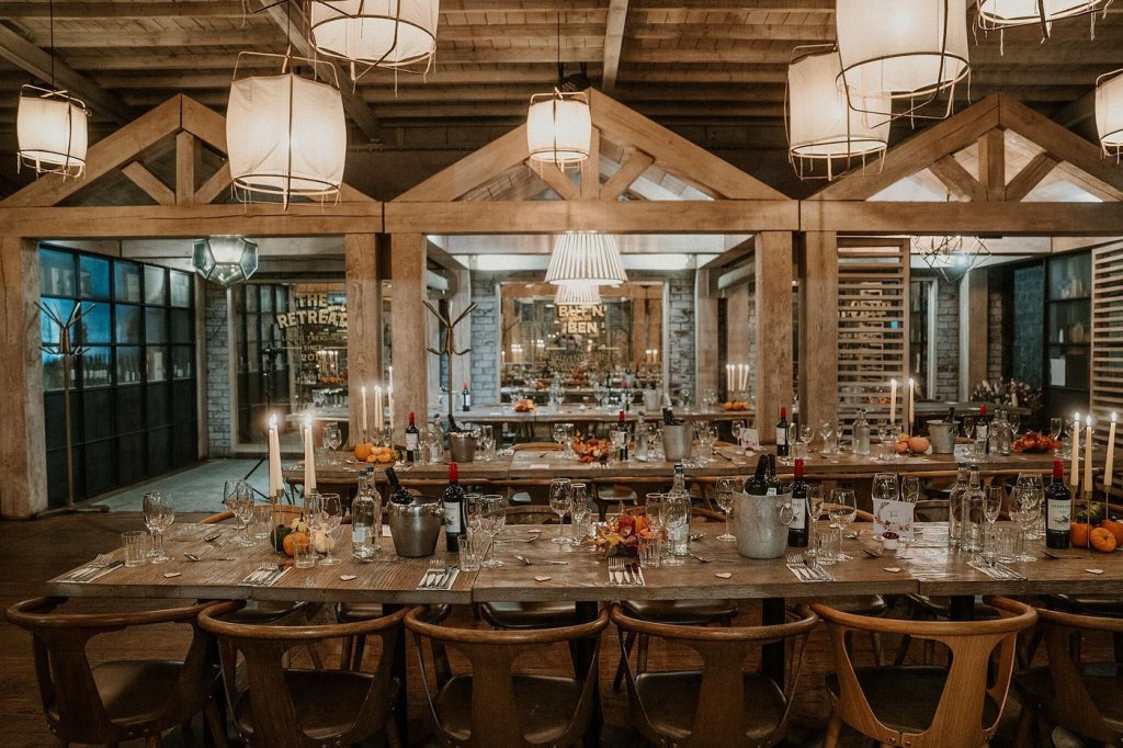 A spacious room with large wooden beams and three long tables with decorative centrepieces to seat up to 12 people lanterns Home from the roof which makes the building feel very premium.